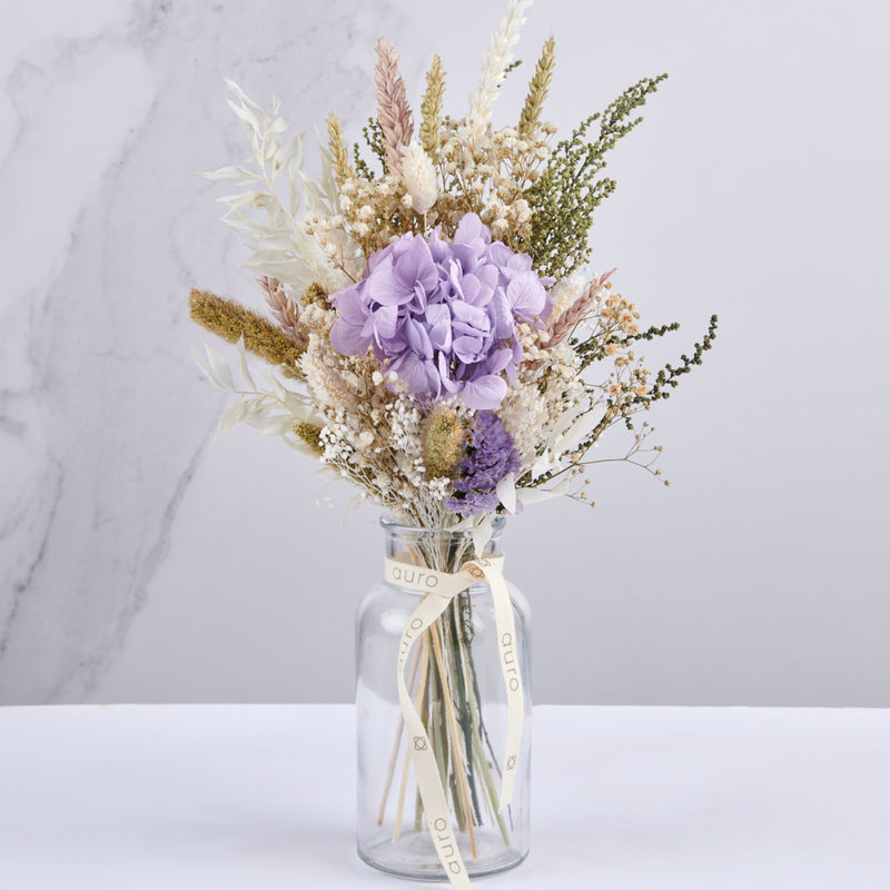 Jarrón de cristal con flores preservadas con hortensias y paniculata.